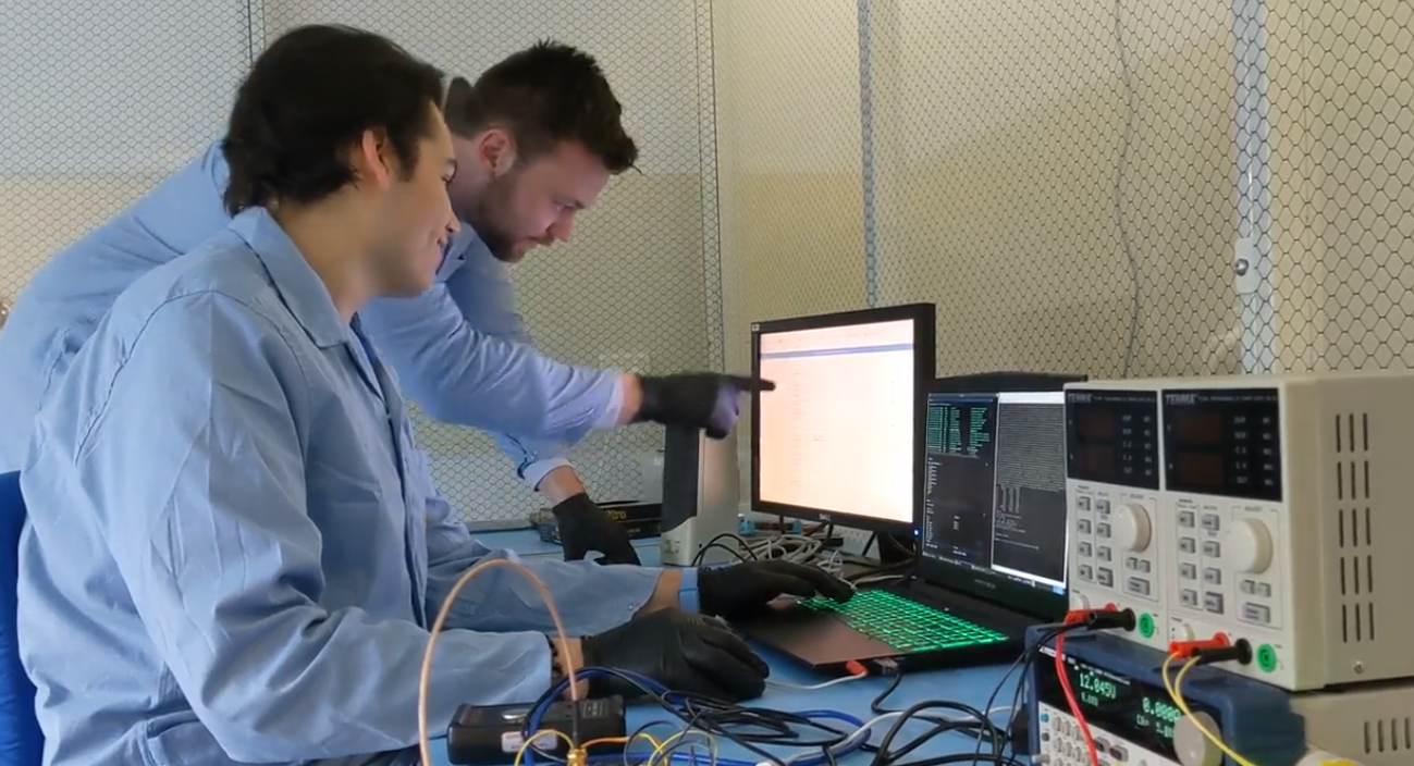 Engineers Daniel Wardle and James Hain surrounded by satellite electronics and checking data on the computer in the clean room